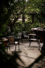 Fototapeta premium Shaded outdoor seating area of a garden cafe with woven chairs and lush green foliage on a stone patio