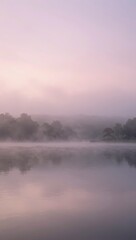 Fototapeta premium Misty Morning Reflection on Calm Lake with Silhouetted Trees in Soft Fog