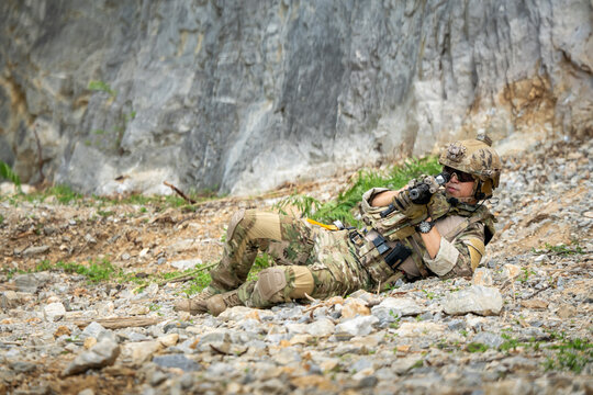 Soldier in camouflage engaged in tactical training rocky terrain action shot outdoor setting ground-level perspective for military awareness