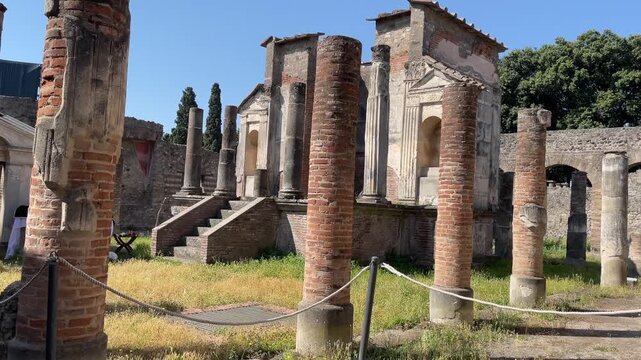 Smooth lateral tracking shot across the remains of a Roman temple and peristyle in Pompeii, featuring weathered brick columns, stone podiums, and archaeological ruins