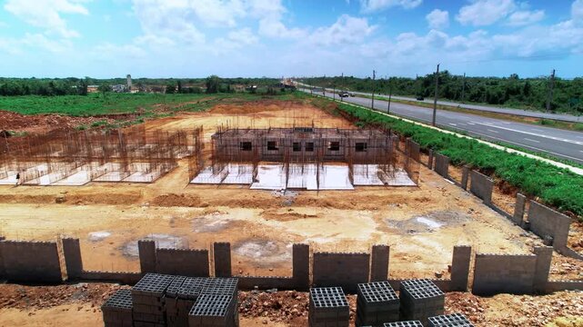 Low-altitude lateral drone tracking shot of a residential construction site, capturing concrete masonry walls, rebar foundation frameworks, and building materials