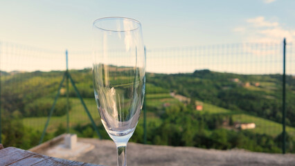 Obraz premium Empty Wine Glass on Terrace Overlooking Lush Green Italian Valley