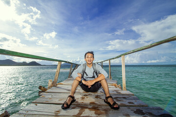 Naklejka premium Happy Traveler Sitting on Wooden Pier Above Tropical Sea