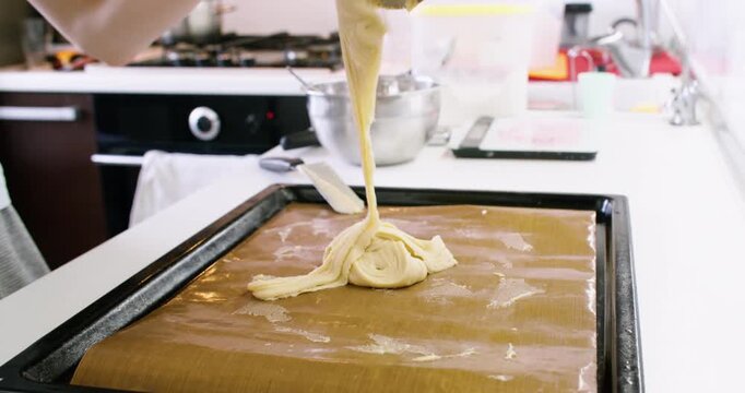 Pastry preparation. Confectionery work. Female baker hand putting sweet dough with spatula on sheet with brown mat kitchen counter.
