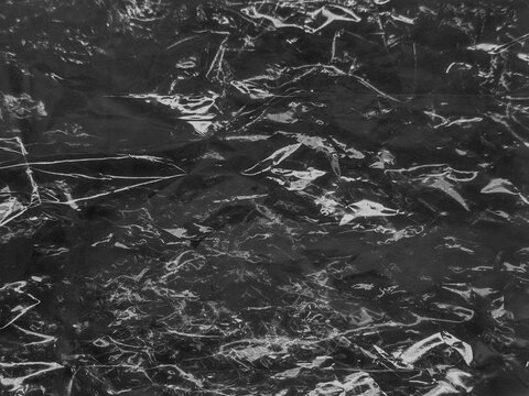 Black crumpled plastic wrap texture with vintage grainy overlay and scratches