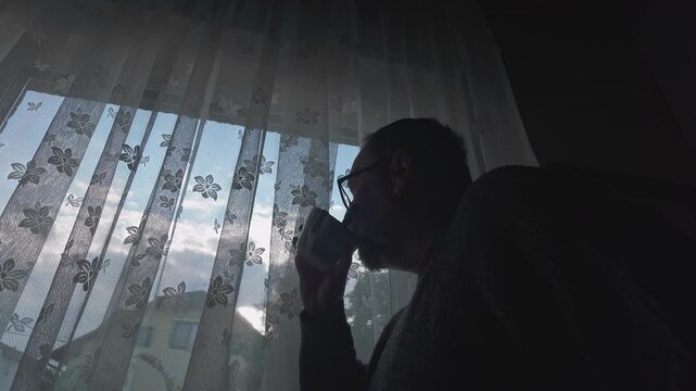 A solitary figure drinks from a cup while gazing through veiled curtains into the morning sky, conveying loneliness, contemplation, melancholy, and emotional isolation.
