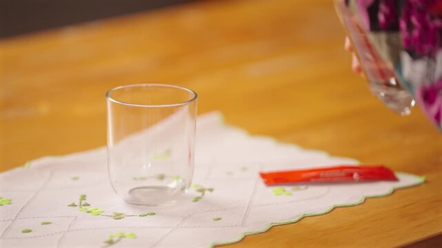 Aged hands pour bottled water and put a vitamin sachet into a clear glass.
