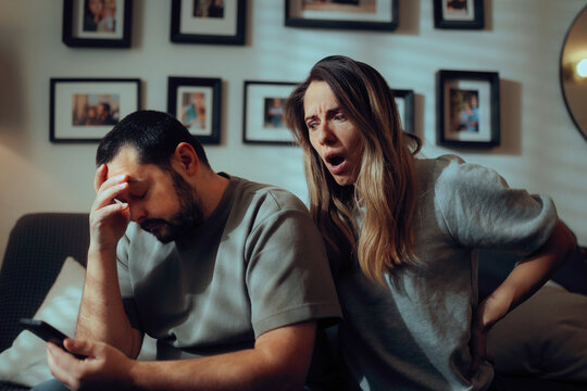 Shocked Woman Checks Phone while Sad Man Regrets Cheating. Surprised girlfriend discovers text messages on boyfriend's smartphone as her boyfriend feels ashamed 