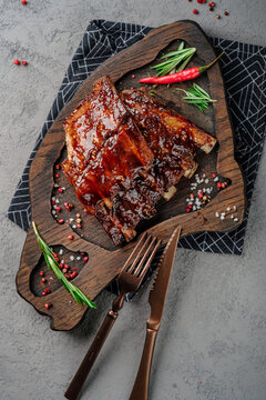 Sticky glazed pork ribs with barbecue sauce, garnished with fresh rosemary and red chili pepper on rustic wooden board. Juicy grilled spare ribs, delicious meat dish, gourmet barbecue style, top view