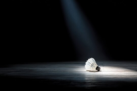 Dramatic badminton shuttlecock under a spotlight on a dark floor