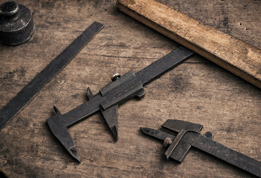 Vintage metal calipers and a wooden ruler resting on a dark rustic wooden table surface used for precise manual engineering measurements