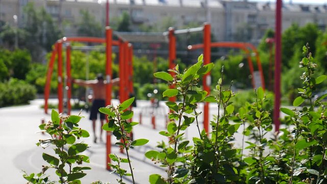 Sports ground in modern residential area, Moscow, Russia. Back view of male athlete outdoors. Blurred man training. Outdoor gym equipment in residential building courtyard. 4 k video
