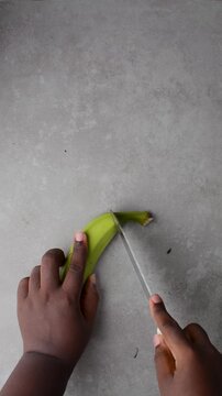 overhead view of Hands peeling unripe plantains, top view of green plantains for frying being peeled, process for making fried plantain