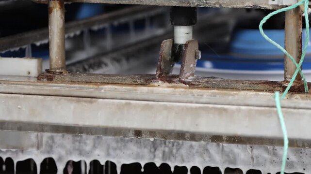 Low-angle close-up of a worn metal machine frame with rusted bolts and a blue rotating part in a dim industrial workspace