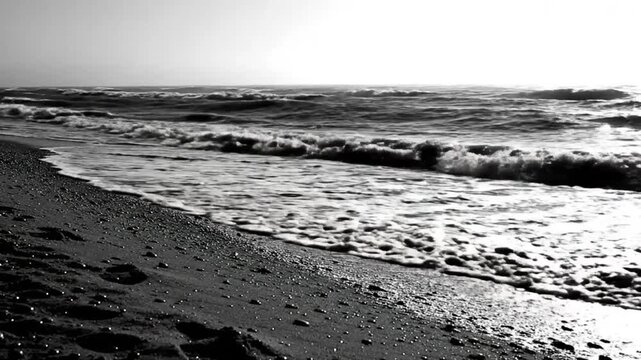 Black and white shot of ocean waves rolling onto a sandy beach in slow motion, natural seascape