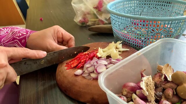Hands Chopping Red Chili, Garlic and Shallots on Wooden Cutting Board in Home Kitchen