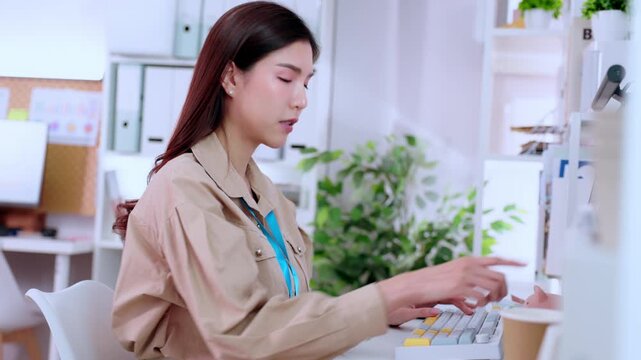 Asian woman using computer keyboard at office desk for business technology work focused employee in modern workplace interior with plant professional worker typing desktop