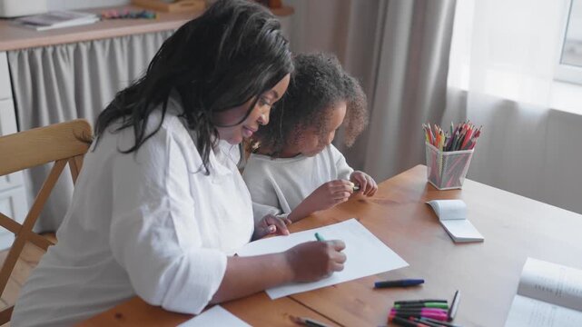 Portrait of cute six-years girl and mother or teacher at home, kids education. African american ethnicity, family time and home education, child studying english or foreign language, development
