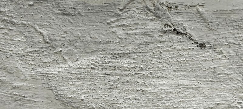 Foto close-up tekstur dinding beton kasar yang bercat putih kusam dengan retakan tipis, cocok untuk latar belakang industri atau grunge.