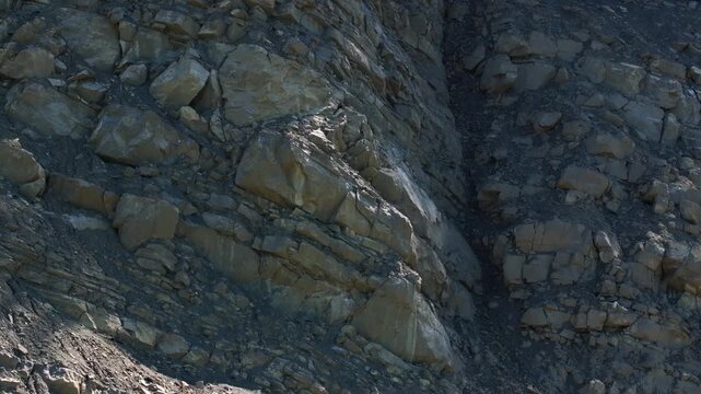 Exposed rock layers and loose rubble on the steep wall of an active quarry. The excavated slope reveals geological strata, fractured stone, and raw mineral deposits in an industrial extraction site.