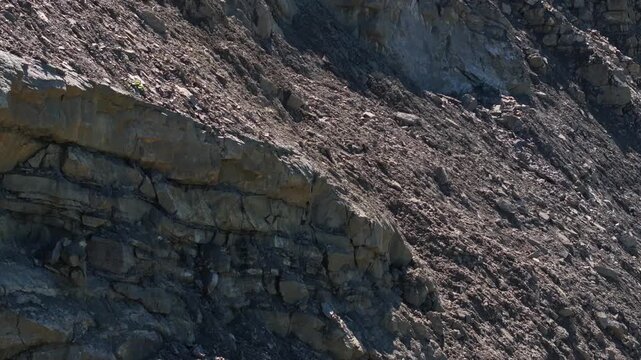 Exposed rock layers and loose rubble on the steep wall of an active quarry. The excavated slope reveals geological strata, fractured stone, and raw mineral deposits in an industrial extraction site.