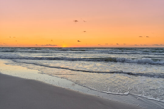 Golden summer sunset over the Baltic Sea with soft waves and sandy shoreline. Tranquil evening seascape with colorful sky and peaceful coastal atmosphere.