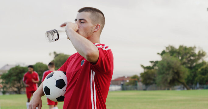 Ball, drinking water and soccer with man outdoor on grass pitch for fitness or hydration. Bottle, space and sports with thirsty football player on field for competition, game or match practice