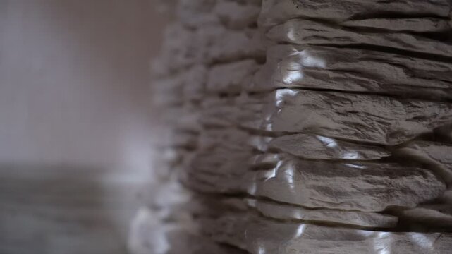 Interior of a modern loft with a white slate stack wall. Sunlight gleams softly on the textured surface, highlighting the natural stone pattern. Spacious and minimalist, copy space for text 