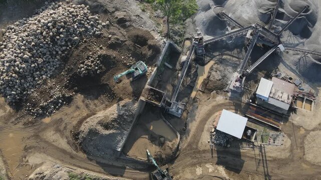 Aerial View of Excavator Processing Ore Near Rock Crusher Facility in Mining Quarry, Construction and mining site view from above.
