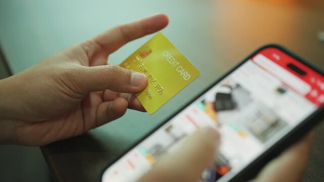 Close-up of a person holding a credit card while shopping online on a smartphone, representing digital payments and e-commerce transactions.