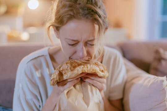 Distressed woman breathing into a paper bag while sitting on a sofa, portraying a candid moment of panic for mental health and anxiety awareness