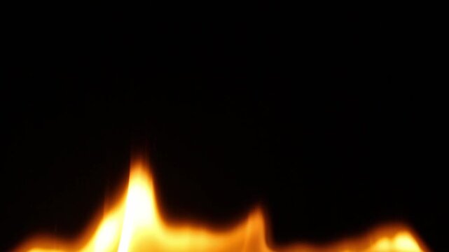 Low orange flames of fire glow along the bottom edge of the dark background, flickering and spreading out to the sides, then rising higher, and then gradually turning into sparks and going out.