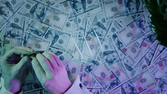 Hand using a credit card to make a line of cocaine on a pile of hundred-dollar bills