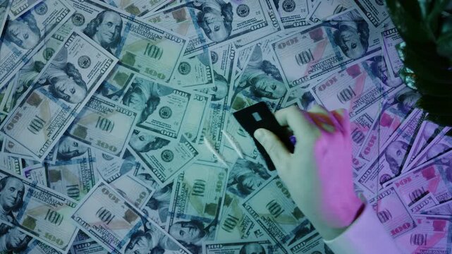 Hand using a credit card to make a line of cocaine on a pile of hundred-dollar bills