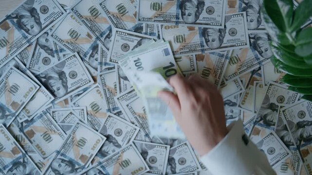 Male hands counting a stack of hundred euro banknotes over a background of one hundred dollar bills