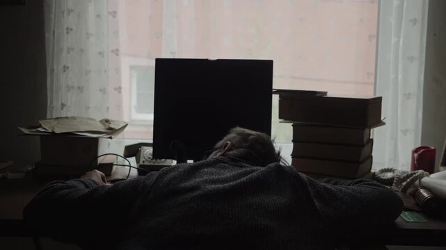 Backlit scene of an exhausted home worker collapsed over a keyboard, highlighting burnout, overwork, and the emotional toll of relentless deadlines.