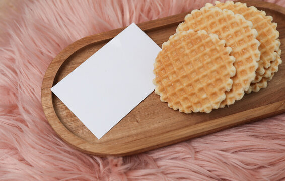 Delicious waffle discs in tray with white business card on pink background