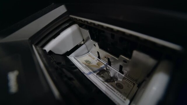 Close-up of a person depositing a stack of hundred-dollar bills into an atm cash slot