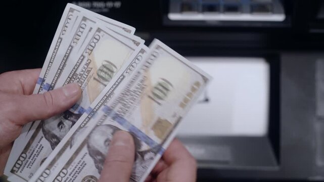 Close-up of male hands counting a stack of us one-hundred-dollar bills in front of a cash deposit