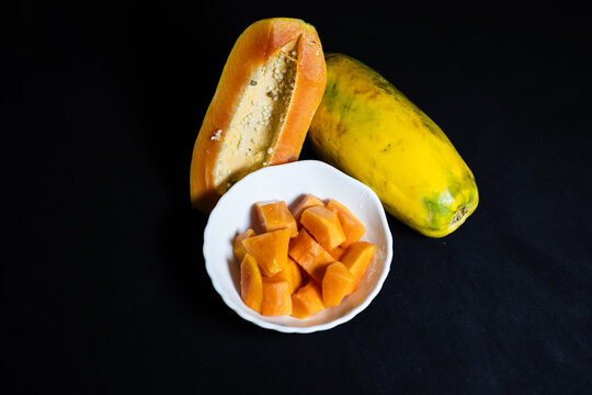 fresh papaya pieces in bowl alongside whole ripe fruit rich in vitamins