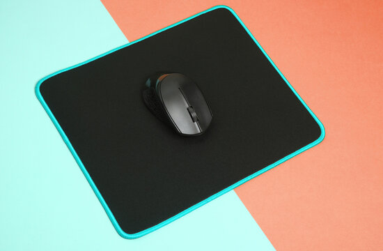 Black PC mouse with PC mouse pad on a pink blue background