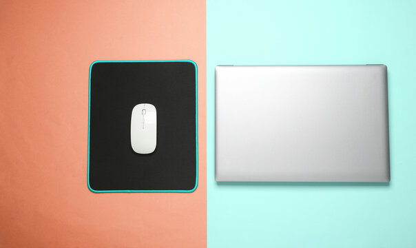 Laptop and PC mouse with PC mouse pad on pink blue background. Top view