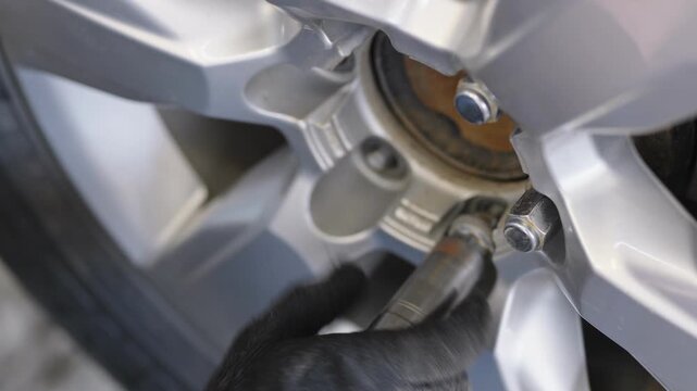 A gloved hand uses a socket wrench to tighten a lug nut on a silver car alloy wheel