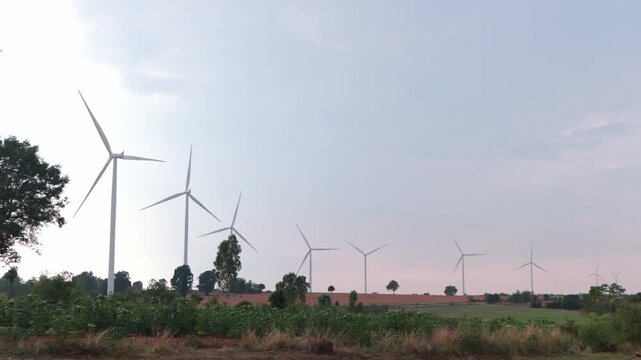 Two Asian male safety engineers working and inspecting sustainable clean power grid inside green wind turbine energy farm. Corporate tech workers checking electric generator outdoor plant.