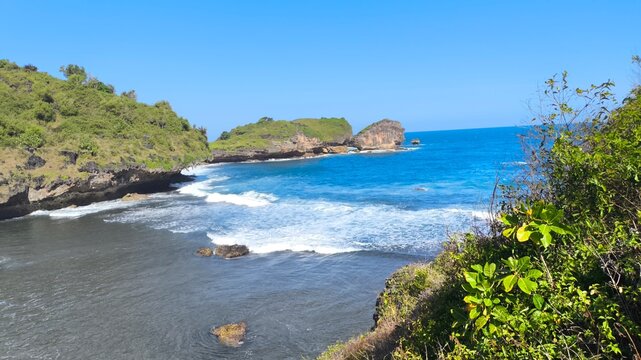Scenic view of Watu Karung Beach in Pacitan with green cliffs, sea waves, and blue sky