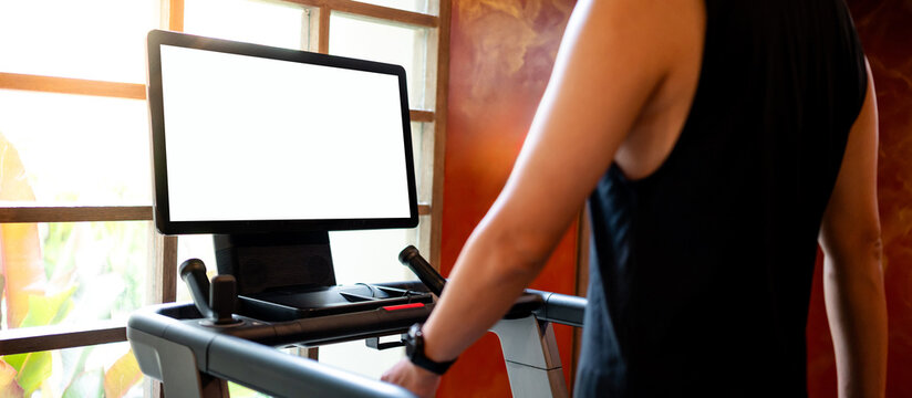Blank white monitor screen on treadmill console with a man running on track. Indoor running machine for cardio workout in fitness gym. Sport equipment technology for athletic performance analytics