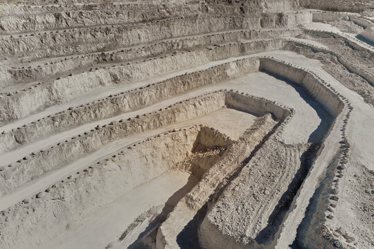 Drone view of a large terraced limestone quarry with winding haul roads and stepped excavation levels. Industrial mining landscape showing mineral extraction, raw materials production and quarry engin
