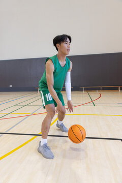Orange basketball bouncing near midcourt on hardwood floor with colored court lines, copy space
