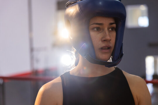 Female boxer pausing in gym boxing ring wearing blue headguard and black top, copy space