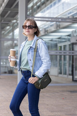 20s female standing near glass entrance wearing sunglasses, olive bag holding stacked to-go cups © wavebreak3